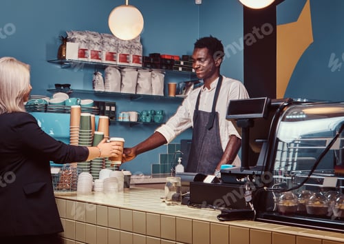 Preview: African American barista in uniform giving a cup of coffee to his client at the trendy coffee shop