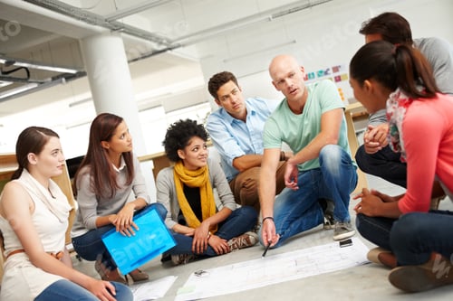Preview: A group of multi-ethnic creatives huddled together and listening to the presentation of a plan