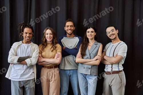 Preview: group photo of happy and stylish multiethnic team with folded arms near black drape in office