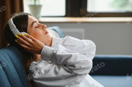 Preview: woman sitting on the couch at home listening to music on headphones technologies