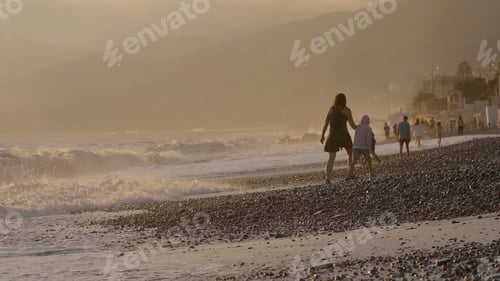 Preview: Waves on pebbled beach during sunset. Creative. Vacation Concept, people walking at the sea shore.