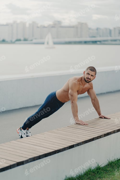 Preview: Determined muscular man warms up before training stands in plank pose