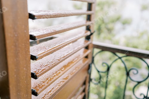 Preview: Raindrops on the slats of brown wooden blinds on a balcony window