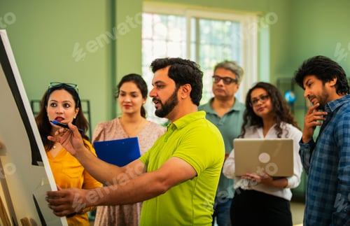 Preview: Confident Indian Asian businessman explaining business strategy to his team using a chart