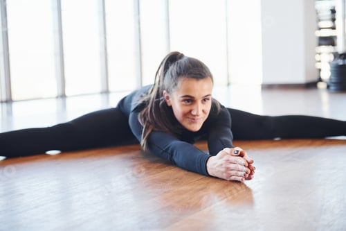 Preview: Sporty woman in black sportswear lying down on the floor by doing stretching