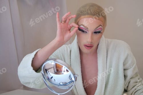 Preview: Drag queen person removing false eyelashes and wearing bathrobe.