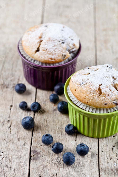 Preview: Two homemade fresh muffins on ceramic green and purple bowls with blueberries.