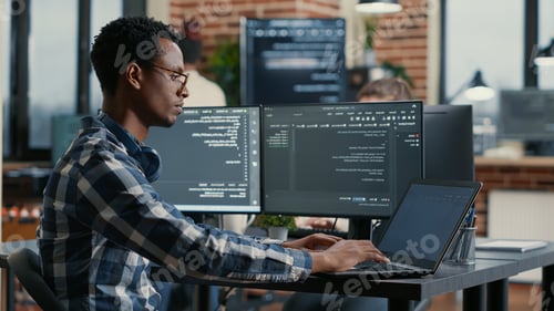 Preview: Portrait of african american developer using laptop to write code sitting at desk with multiple
