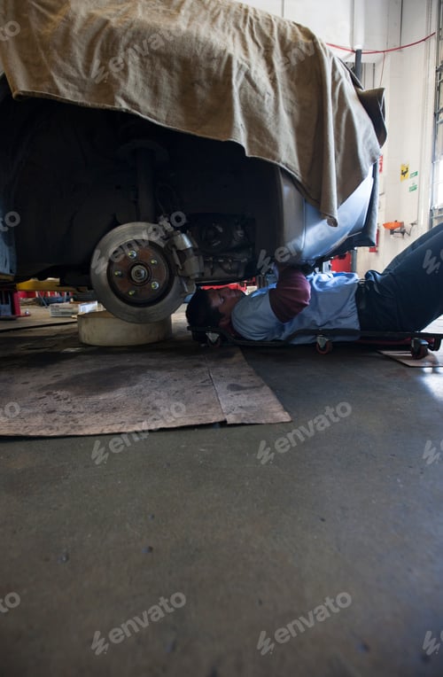 Preview: Mechanic lays on a trolley under a car in an auto repair shop