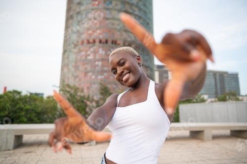 Preview: Smiling black woman framing with hands in barcelona cityscape with agbar tower