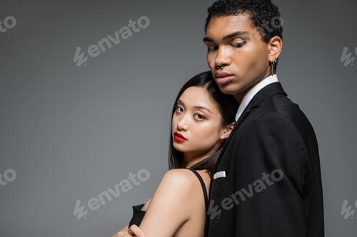 Preview: charming asian woman with red lips leaning on african american man in black blazer isolated on grey