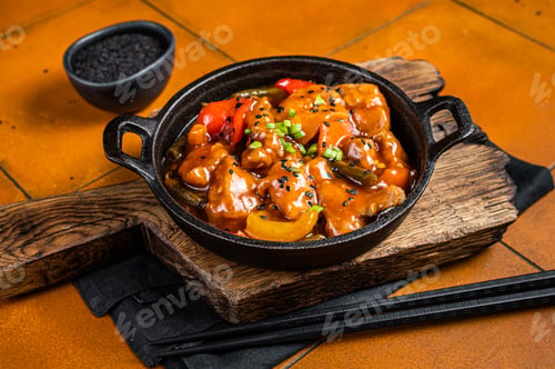 Preview: Chinese Sweet and sour chicken with colorful bell pepper in a skillet. Orange background. Top view