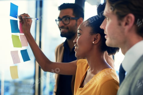Preview: Cropped shot of a group of businesspeople brainstorming with notes on a glass wall in an office