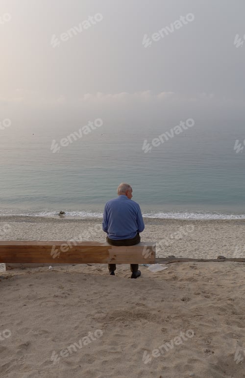 Preview: Man sitting on a beach bench with ocean waves in the background