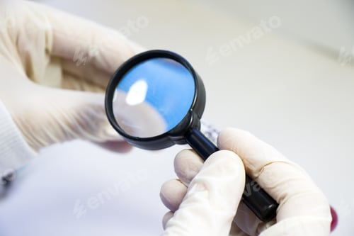Preview: Closeup shot of the magnifying glass and human hands analyzing the test results