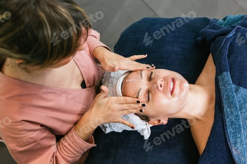 Preview: Crop beautician cleansing face of woman in salon