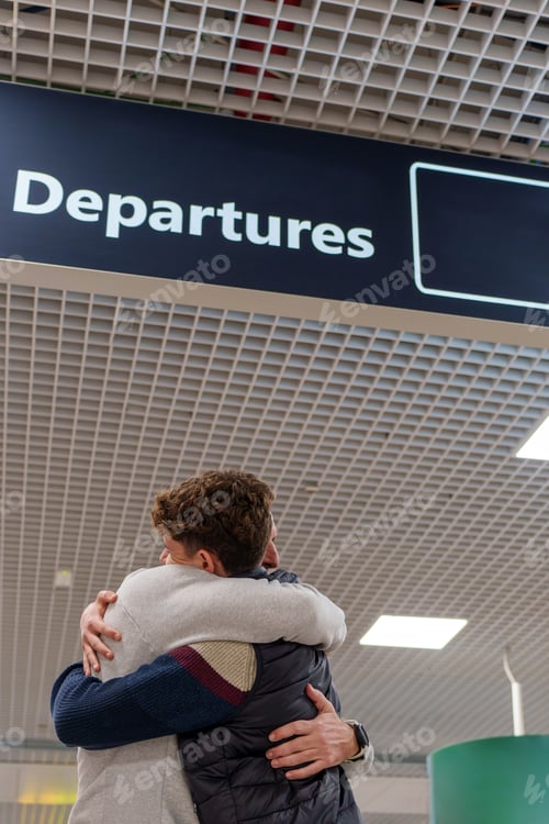 Preview: Father and son embracing at the airport under the departures sign, saying goodbye before a journey