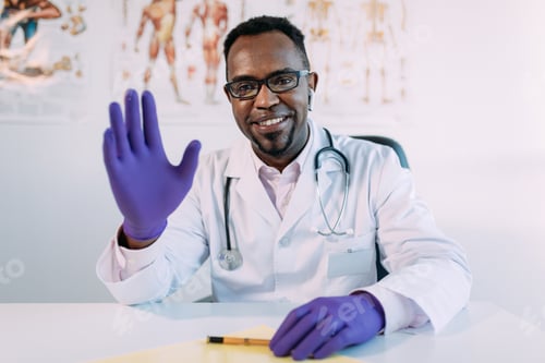 Preview: Friendly young black male physician waving hand and smiling at camera