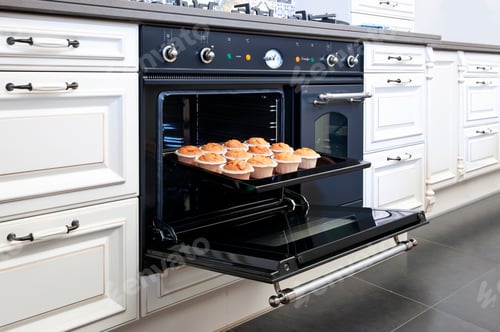Preview: Stylish oven in a modern kitchen, door open with fresh baked cup cakes on a baking tray.