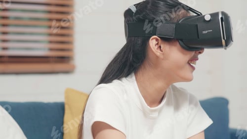 Preview: Asian teenager woman using glasses virtual reality simulator playing video games in living room.