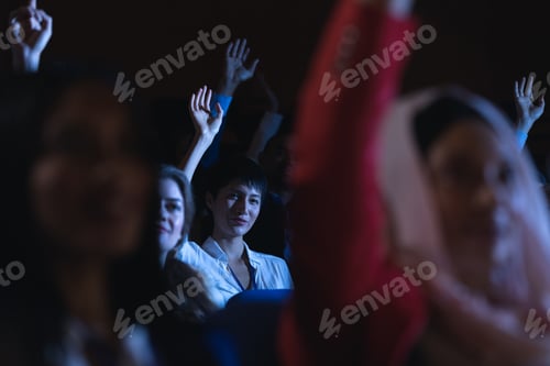 Preview: Low angle view of beautiful Asian businesswoman sitting and raising hand while sitting in auditorium