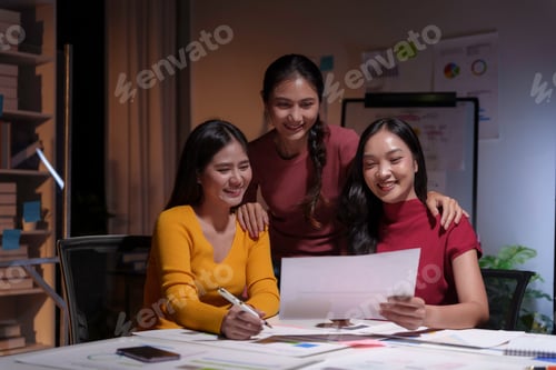 Preview: Three asian businesswomen are working late in their office reviewing a document together and smiling