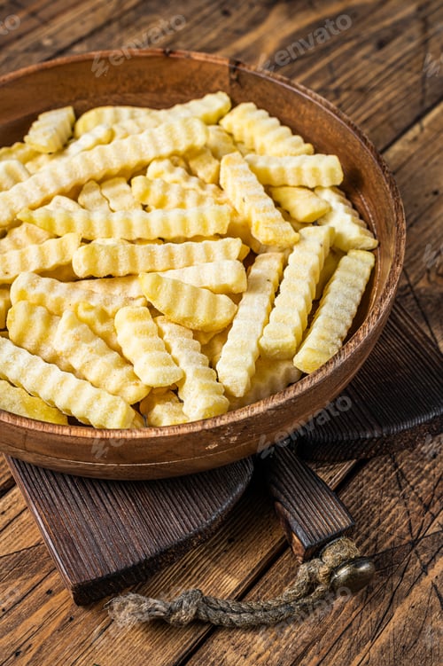 Preview: Frozen Crinkle oven French fries potatoes sticks in a wooden plate. Wooden background. Top view
