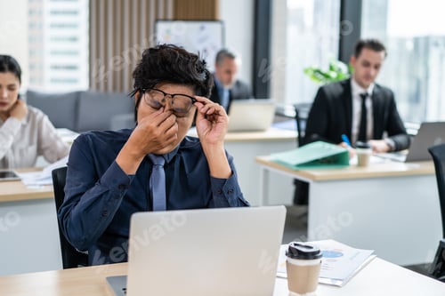 Preview: Exhausted Asain business man using laptop computer working in office.