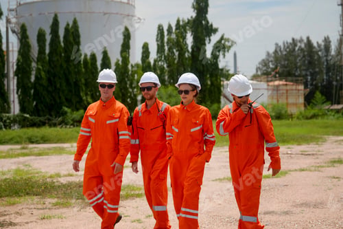 Preview: Workers in orange uniforms walk through an industrial area during a sunny day