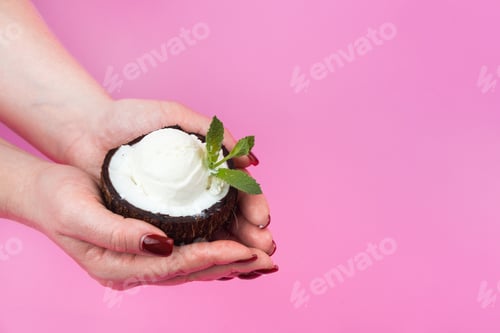 Preview: Vanilla ice cream balls in a fresh coconut half, decorated with mint leaves in your hand on a pink