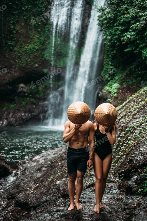 Preview: A man and a woman in conical hats at a waterfall. The couple travels the world. Vacation in Asia