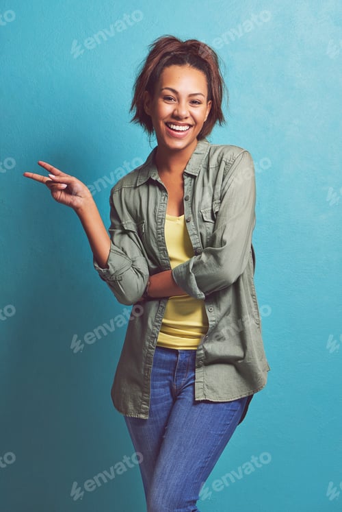 Preview: I come in peace. Portrait of a young woman showing you the peace sign against a blue background.
