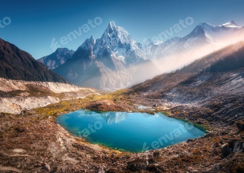 Preview: Snowy mountain with illuminated peaks and small lake at sunrise