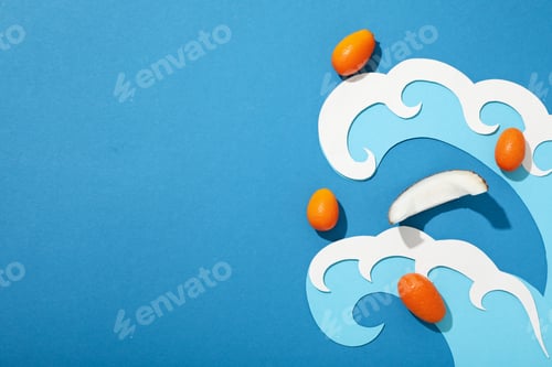 Preview: Piece of coconut, whole kumquats and paper waves on blue background, space for text