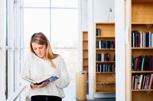 Preview: Young woman reading book in library