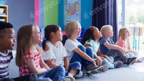 Preview: Group Of Smiling Elementary School Pupils Sitting On Floor In A Line Listening To Teacher