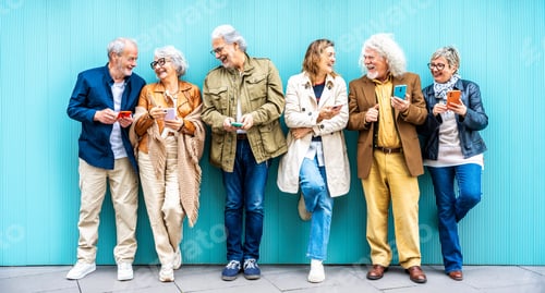 Preview: Group of senior people using technology devices together standing on a blue wall