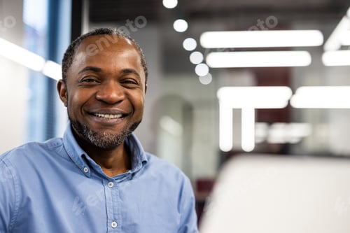 Preview: Smiling business professional in blue shirt working at modern office desk with bright lighting