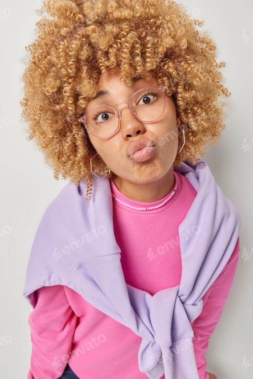 Preview: Photo of lovely curly haired woman keeps lips rounded sends mwah at camera has romantic mood wears