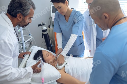 Preview: Side view of diverse doctors using defibrillator on Asian female patient in ward at hospital