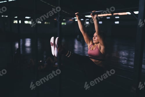 Preview: Muscular young woman doing pull ups during intensity crossfit exercising with endurance