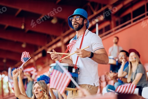 Preview: Happy sports fan cheering for USA while playing drums at stadium stands.