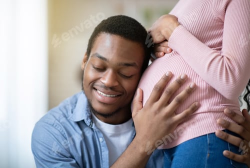 Preview: Young black man pressing his ear against his wife's pregnant belly, listening to his baby's