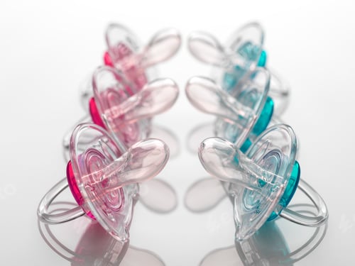 Preview: A collection of colorful pacifiers arranged in a circle on a reflective surface.
