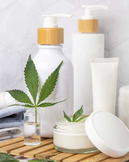 Preview: Opened cream jar with white lid near green cannabis leaves close up, CBD cosmetic mockup