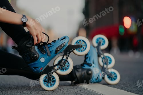 Preview: Woman puts on rollerblades poses outdoors on asphalt against blurred background.