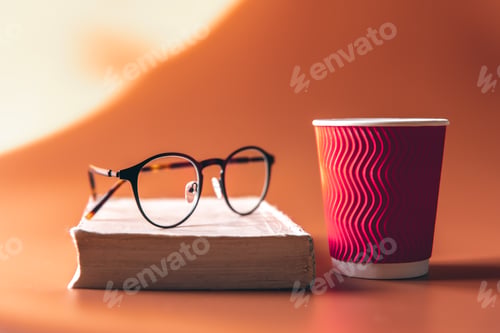 Preview: Glasses, a book and a paper glass of coffee.