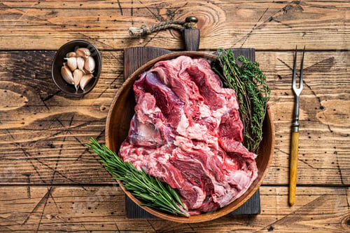 Preview: Boneless raw mutton Lamb Shoulder meat in wooden plate with herbs. wooden background. Top view