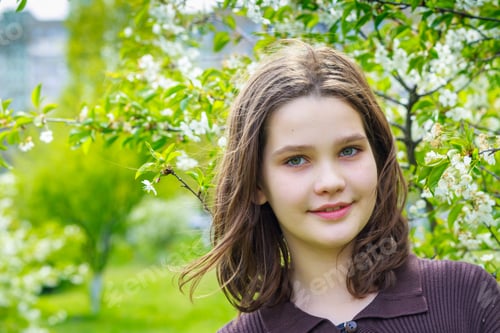Preview: Beautiful girl among cherry flowers in spring. Portrait of a girl with brown hair and green eyes.