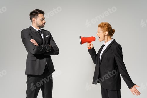 Preview: angry businesswoman screaming in megaphone at confident man in suit standing with crossed arms